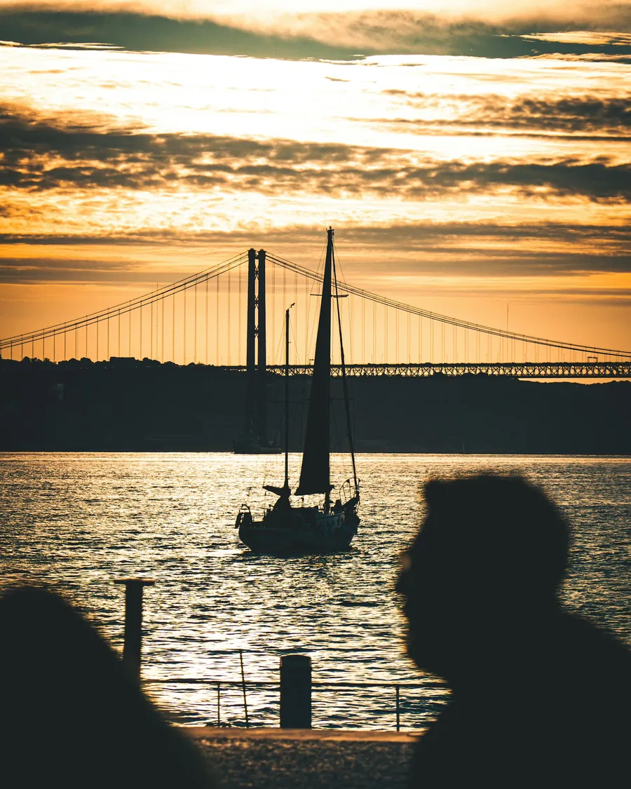 A sailing boat on the Tagus at sunset, with the 25 de Abril bridge behind
